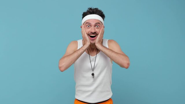 Shocked amazed young fitness man thin skinny body sportsman in headband shirt isolated on blue background. Workout gym sport motivation concept. Look camera keep mouth open say wow put hands on head