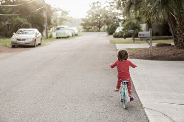 A five year old boy in a red shirt riding his bike on a quiet residential street. 