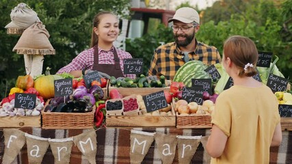 Happy male farmer with his teenage daughter talking to the buyer when trading vegetables and fruits at the farmers market