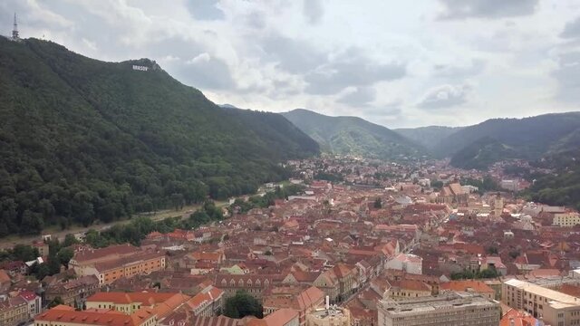 Aerial view of Brasov city, medieval town situated in Transylvania, Romania. Old architecture surrounded with big Carpathian mountains covered with dense green forest.