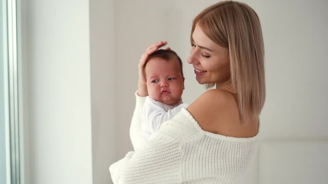 young beautiful woman holds a newborn baby in her arms walking around the room hugs and kisses