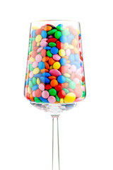 A wine glass full of colorful chocolate dragees, isolated on white. Studio photo. Selective focus.