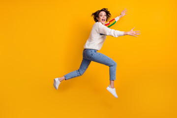 Profile full size photo of optimistic funny girl run hug friend wear rainbow sweater denim jeans white shoes isolated on yellow background