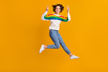 Profile full size photo of cheerful funny young woman jump show v-sign wear sweater jeans footwear isolated on yellow background