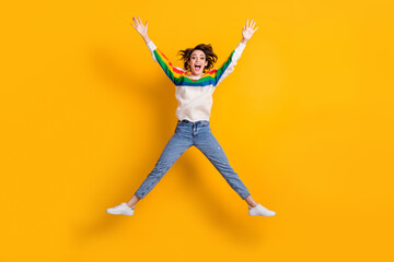 Fototapeta na wymiar Full size photo of cute crazy young woman jump like star wear rainbow sweater denim jeans white footwear isolated on yellow background