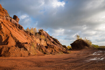 Red mountains with autumn trees and blue cloudy sky. Colored waste heaps after extracting coal from mines.