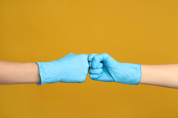 Doctors in medical gloves making fist bump on yellow background, closeup