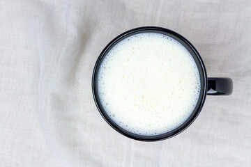 Top view of milk in black ceramic cup on white cloth background with copy space. 