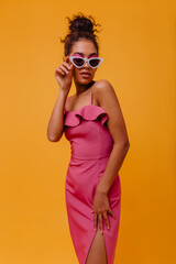 Serious graceful girl in pink dress looking down. African fashionable woman posing in sunglasses.