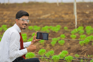 Fototapeta premium Technology and people concept, Young indian agronomist using tablet or smartphone at greenhouse