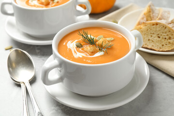 Tasty creamy pumpkin soup with croutons, seeds and dill in bowl on light grey table