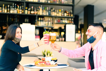Happy friends having a party drinking cocktails at bar - Fashionable teenagers celebrating in a coffee bar drinking alcohol - New normal lifestyle concept about face mask