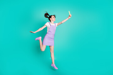 Full length body size photo of brunette girl with tails jumping high taking selfie smiling isolated on vibrant teal color background