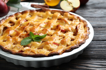 Traditional apple pie with mint on black wooden table, closeup