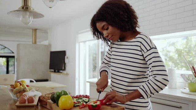 Young woman alone in the modern kitchen cutting red bell pepper with a knife on chopping board