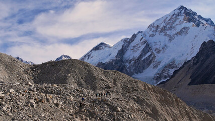 People hiking through the rock-covered majestic Khumbu glacier on the way to village Gorakshep on Everest Base Camp Trek with snow-capped Nuptse in the Himalayas, Sagarmatha National Park, Nepal.