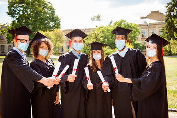 Photo portrait of six graduates showing diplomas wearing face masks outside