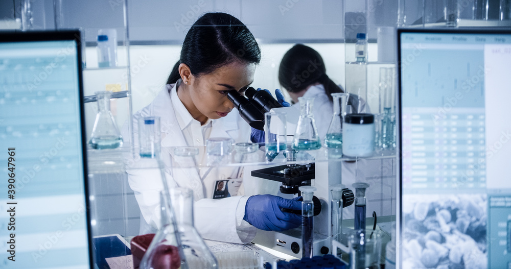 Wall mural multi ethnic science team working with microscope and computer. female doctors in futuristic laborat