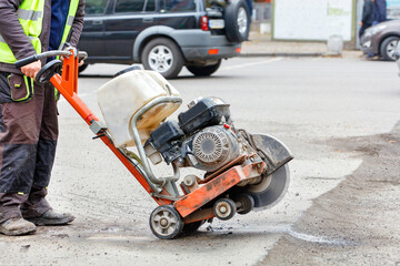 Obraz premium A worker moves a petrol cutter with a working diamond cut-off wheel to a bad section of the road that needs repair.
