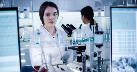 Multi ethnic science team working with microscope and computer. Female doctors in futuristic laboratory. Smiling at camera