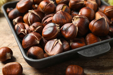Delicious roasted edible chestnuts in baking dish on wooden table, closeup