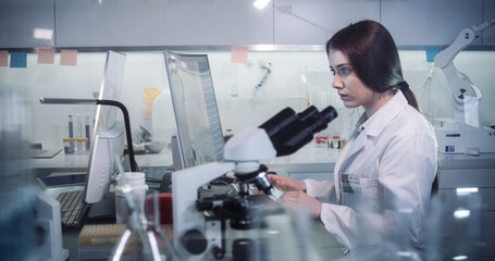 Young female doctor working with microscope. Close up on face. Futuristic laboratory interior