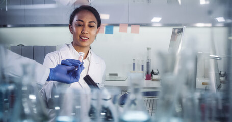 Asian female doctor working in futuristic laboratory. Using microscope and computer for blood samples testing