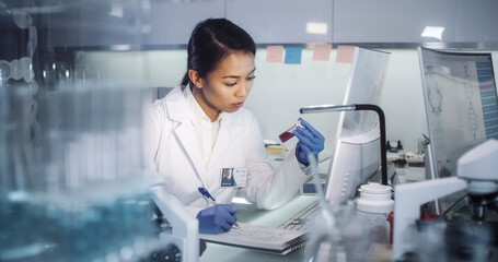 Asian female doctor working in futuristic laboratory. Using microscope and computer for blood samples testing