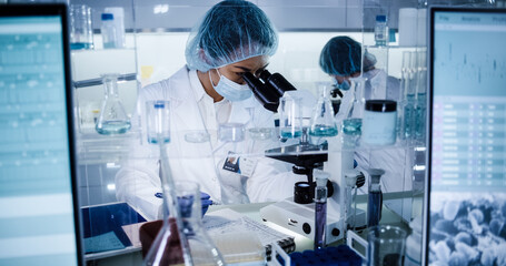 Female science team working on biohazardous samples. Using microscope and computer with data