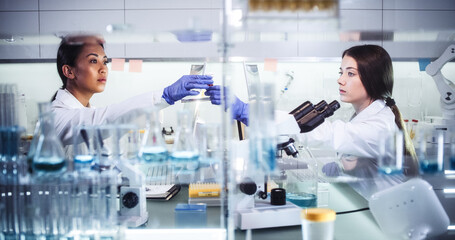 Female doctors testing samples in futuristic laboratory. Using microscopes and computer with data