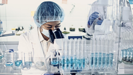 Asian female doctor working with biohazardous samples. Using microscope in futuristic laboratory