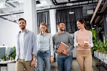 Smiling multicultural businesspeople with coffee to go and paper folder in office