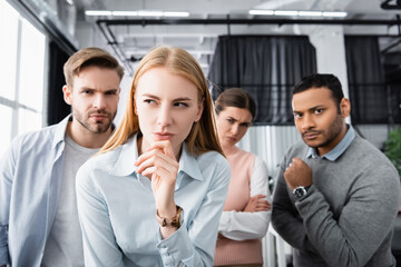 Obraz premium Pensive businesswoman standing near multiethnic colleagues on blurred background in office