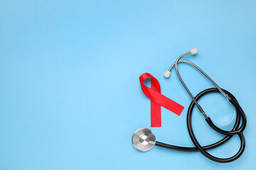 Red ribbon and stethoscope on light blue background, flat lay with space for text. AIDS disease awareness