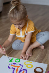 Little preschool child girl sitting on warm floor and painting numbers with paints.