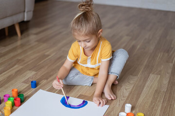 Child sitting on floor and paint with gouache colours. Education concept.