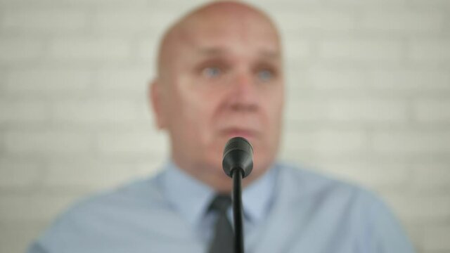Blurred Image of a Businessman Speaker in a Press Conference Talking at the Microphone and Gesturing