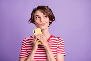 Photo of thoughtful cute lady hold telephone look empty space wear striped t-shirt isolated purple color background