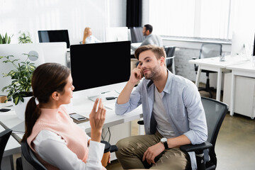 Fototapeta premium Businessman looking at colleague with coffee to go near devices in office