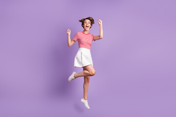 Full length photo of lady jump raise fists open mouth wear striped t-shirt short skirt sneakers isolated purple color background