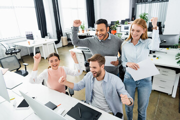 Obraz premium Cheerful multiethnic businesspeople with digital tablet and papers standing near computer in office
