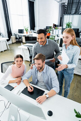 Fototapeta premium Smiling multicultural businesspeople using graphics tablet and computer while working together in office