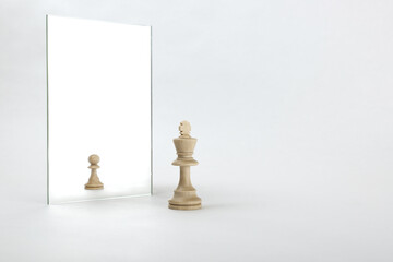 the king is reflected in the mirror as a pawn on white background. underestimation of their...