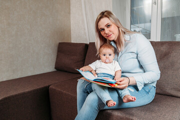 young mum is reading a book with her cute son sitting on the couch