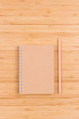 Closed blank spiral notepad and pencil on bamboo table. Top view. Minimal style