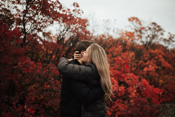 Side view of a lovely young happy couple embracing in colourful red autumn park. 