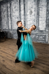 a young man in a black suit is dancing with a girl in a turquoise dress in the dance hall