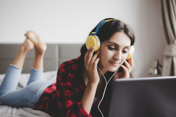 Beautiful woman listening music on laptop computer on bed at home or she watching movie on website by using internet online service and wireless, she wears headphones. Pretty girl get relax and happy