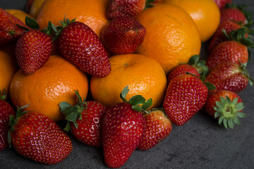 Strawberries and oranges on dark grey background. Fruits top view photo.  Fruit diet concept. 
