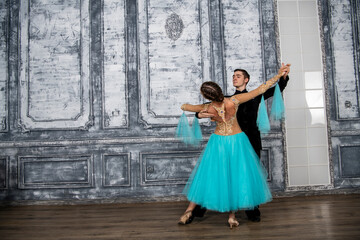 Fototapeta na wymiar a young man in a black suit is dancing with a girl in a turquoise dress in the dance hall